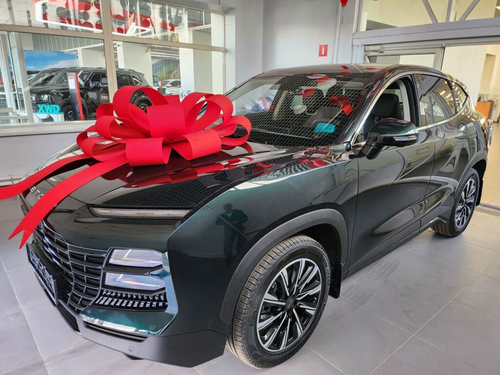 Shiny new SUV featuring a large red bow displayed in a modern car showroom.